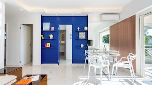 Ein modernes Interieur mit blauer Akzentwand, einem Essbereich mit weißen Stühlen und einem Glastisch.