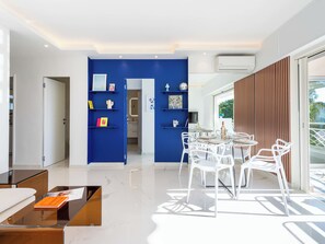 Ein modernes Interieur mit blauer Akzentwand, einem Essbereich mit weißen Stühlen und einem Glastisch.