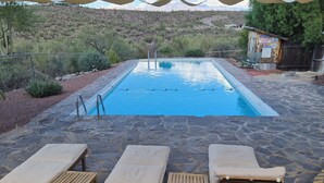 Area piscina con sedie a sdraio e un tavolo in legno sotto una tettoia.