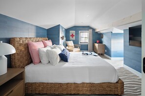 Een slaapkamer met een groot bed, een nachtkastje, een stoel, een klein bureau en een raam met gordijnen.