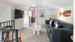 A modern living room with a flat-screen TV, a black leather sofa, and a patterned carpet. - New Crow’s Nest Ocean View l Downtown l Queen Suite (Newburyport)