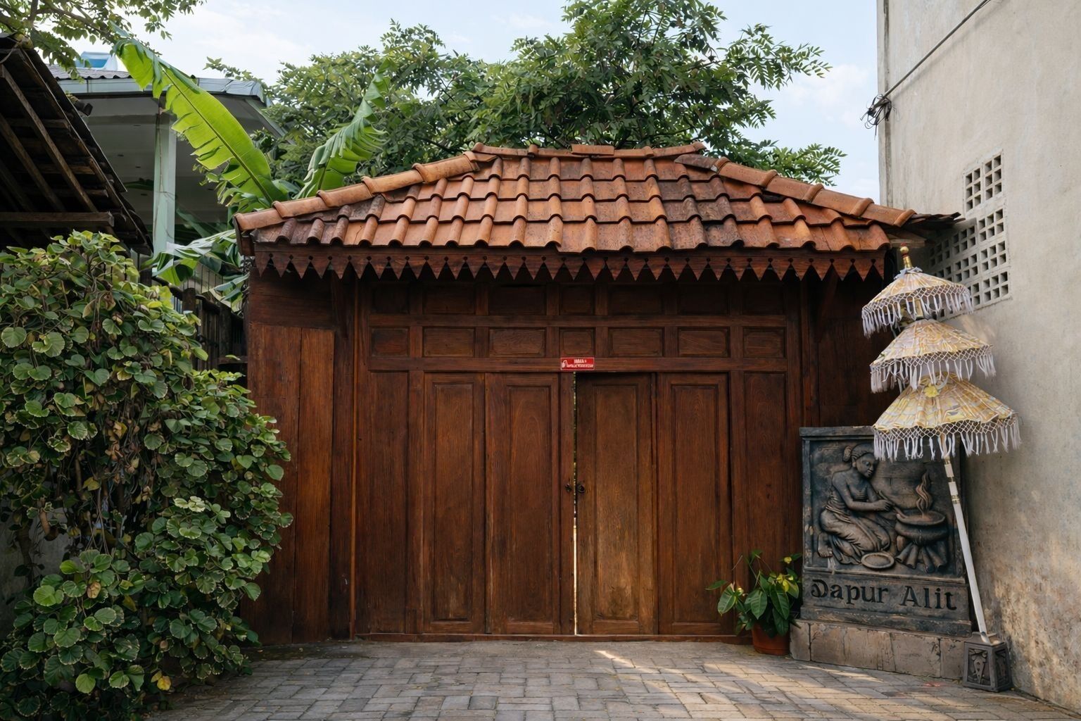 A traditional wooden gate with a tiled roof, a potted plant, and a statue of a seated figure.
