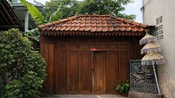 A traditional wooden gate with a tiled roof, a potted plant, and a statue of a seated figure.