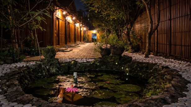 A nighttime garden with a pond, wooden buildings, and a pathway leading to a door. - Dapur Alit Villas (Kasihan)