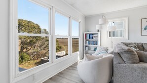 A modern living room with a large window, a gray sofa, a white armchair, and a bookshelf. - "Once in a Blue Moon - 796 OBW" 4 Bedroom, Second Row (Supply)