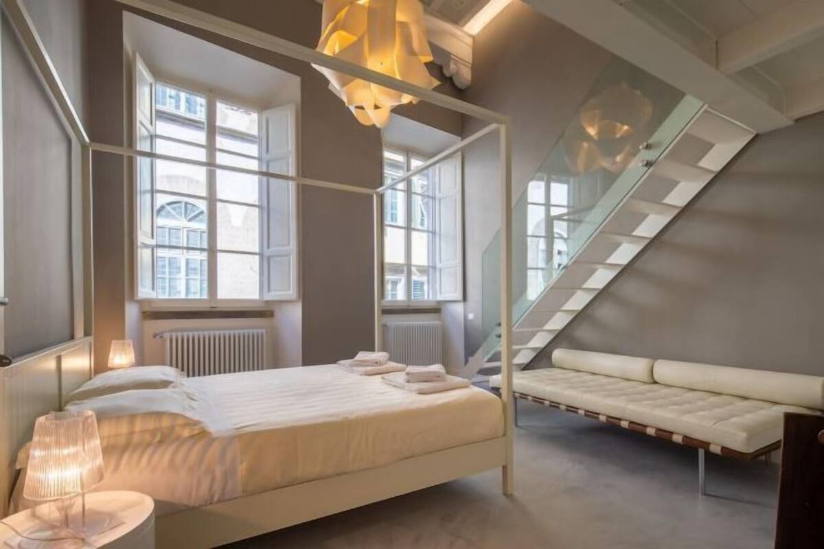 Ein modernes Schlafzimmer mit einem Himmelbett, einer Couch und großen Fenstern.