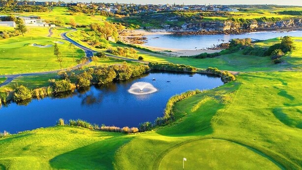 Golfkenttä, jossa on lampi, näkymät merelle ja taustalla asuinalue.