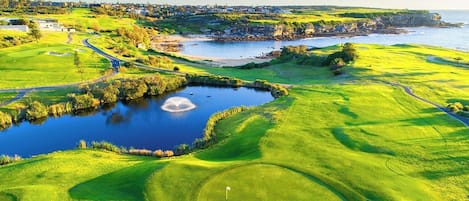 Un parcours de golf avec un étang, une vue sur la côte et une zone résidentielle en arrière-plan.