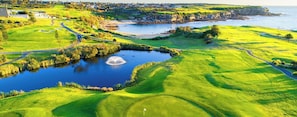 Ein Golfplatz mit Teich, Blick auf die Küste und Wohngebiet im Hintergrund.