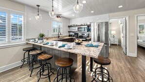 A modern kitchen with a large island, bar stools, stainless steel appliances, and pendant lighting.