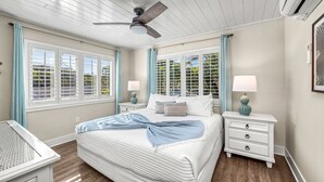 A bedroom with a bed, two nightstands, a ceiling fan, and large windows with curtains.