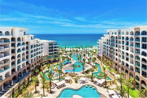 Un resort con diversi edifici, una zona piscina centrale e vista sull'oceano.