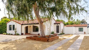 Una casa de dos pisos con techo de tejas, un árbol grande en el jardín delantero y un jardín bien cuidado.