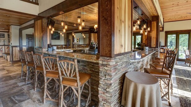 Eine rustikale Bar mit Steinwänden, Holzsesseln und hängenden Pendelleuchten.