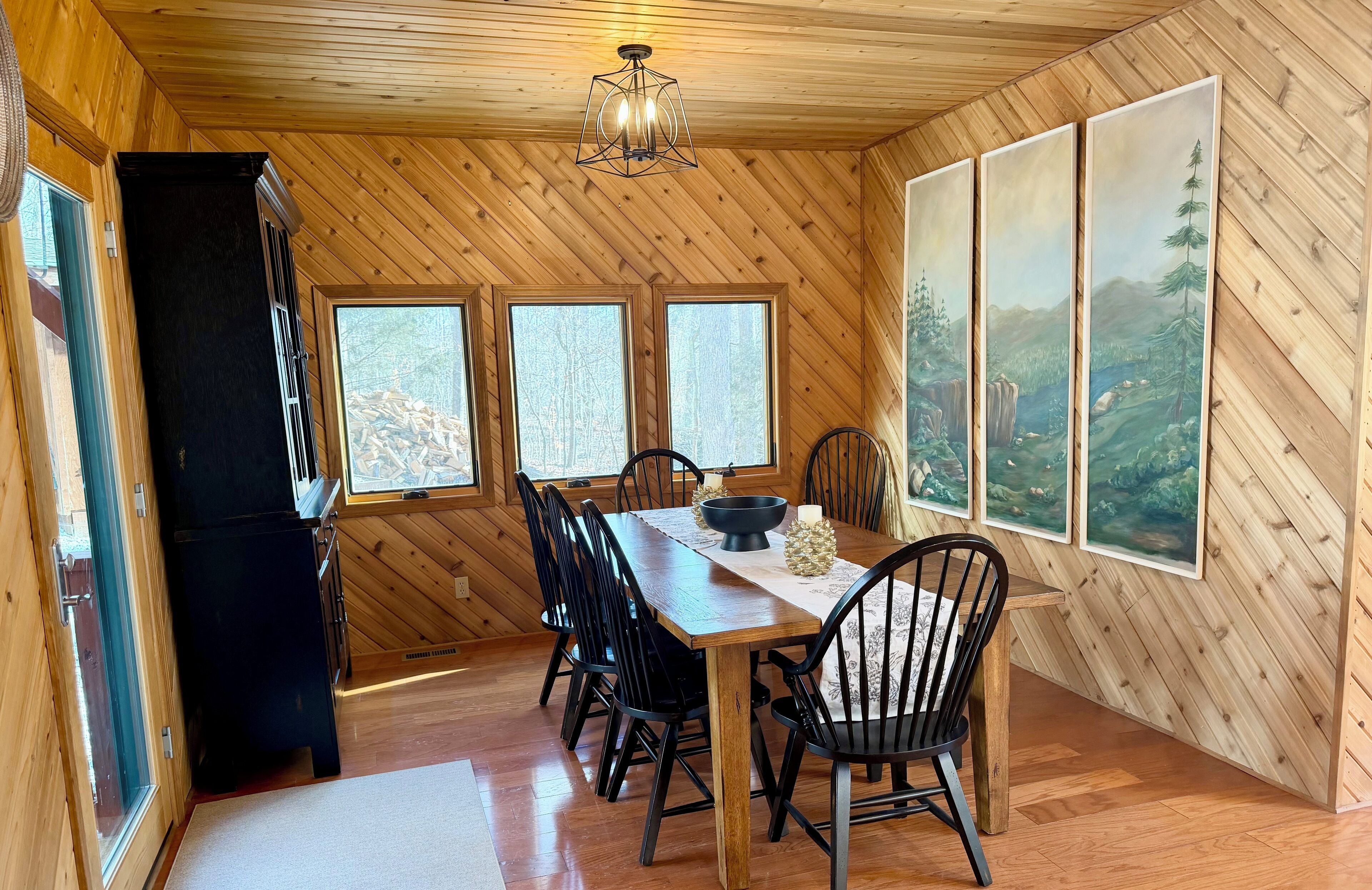 A wooden-paneled dining room with a table, chairs, and a black refrigerator.