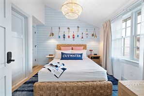 Un dormitorio con cama, una mesita de noche, una lámpara de pared, una ventana con cortinas y una pared decorada con motivos náuticos.