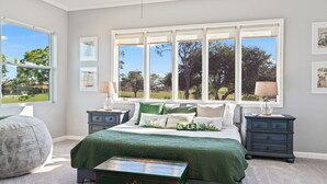 Ein Schlafzimmer mit großem Fenster, einem Bett mit grüner Bettwäsche, zwei Nachttischen und einer Kommode.