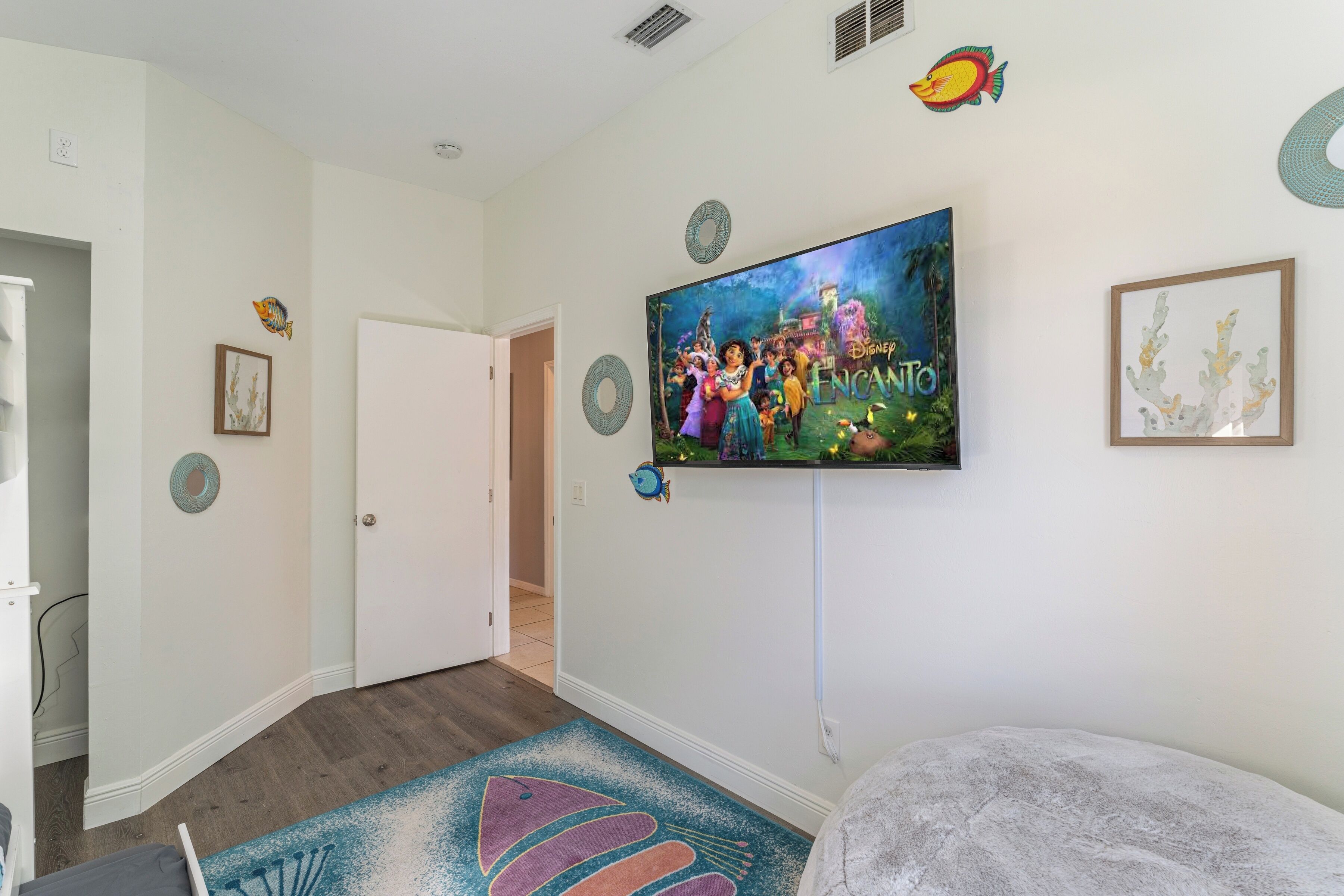 A room with a large Disney-themed poster, a white door, and a colorful rug.