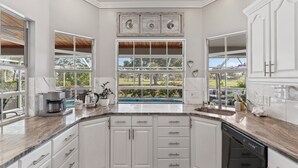 Eine Küche mit weißen Schränken, einem großen Fenster mit Blick auf einen Pool und einer Kaffeemaschine auf der Arbeitsfläche.
