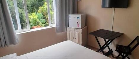 A bedroom with a bed, a TV, a small table, and a window with curtains.