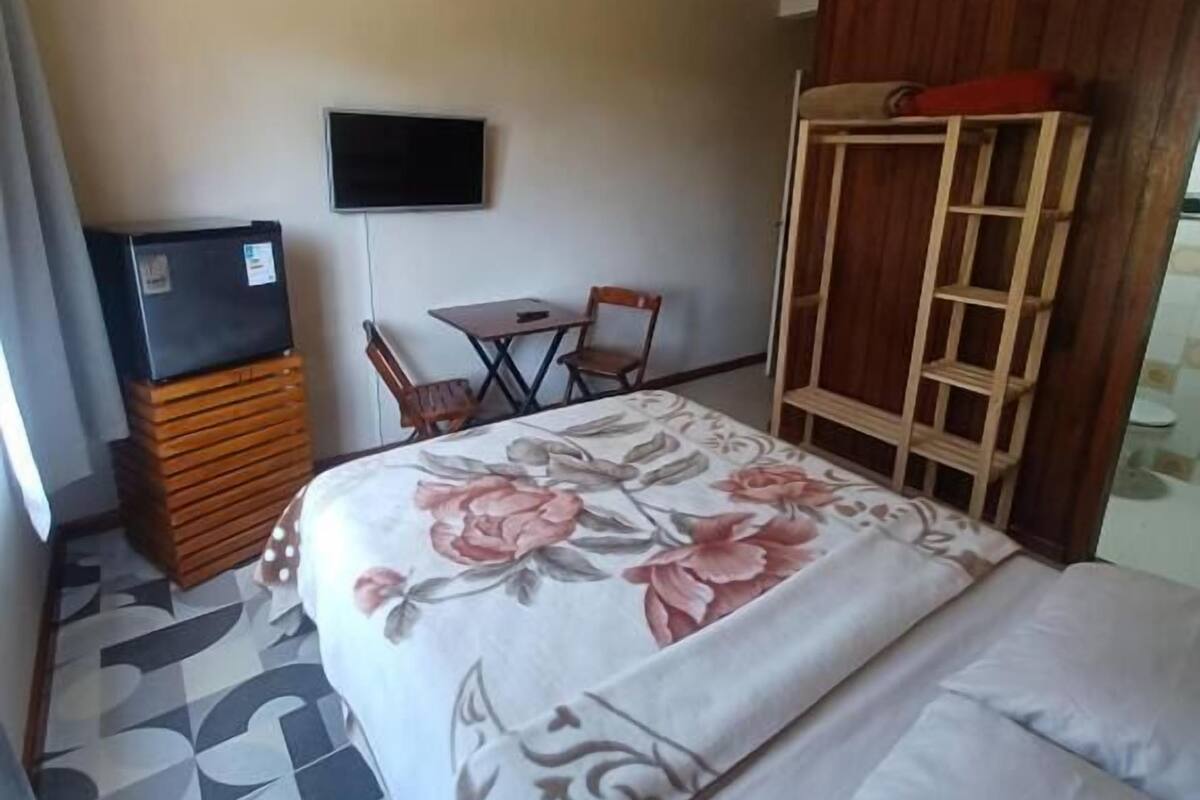 Quarto de hotel com cama, televisão, escrivaninha e cadeira.