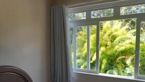 Une chambre à coucher avec un lit, une fenêtre avec des rideaux et une vue sur la verdure.