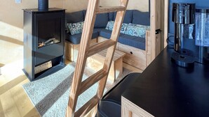 Un intérieur moderne avec un plafond de style industriel, un poêle à bois, une échelle en bois et un ensemble de canapés.
