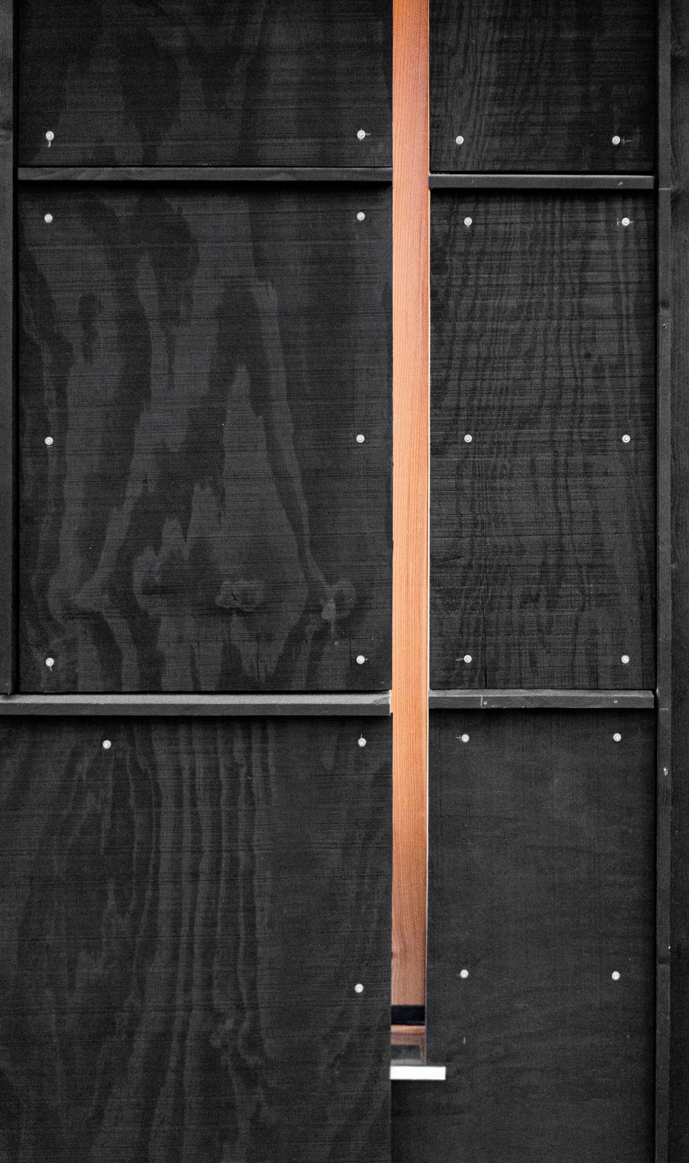 A black wall with a wooden panel and metal studs.
