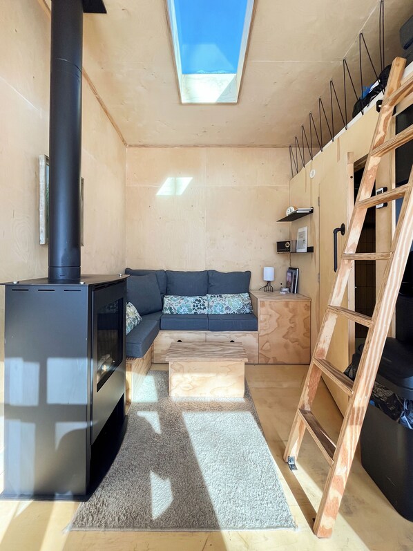 Un espacio habitable moderno con una estufa de leña, un sofá, una mesa de centro de madera, una escalera y un tragaluz.