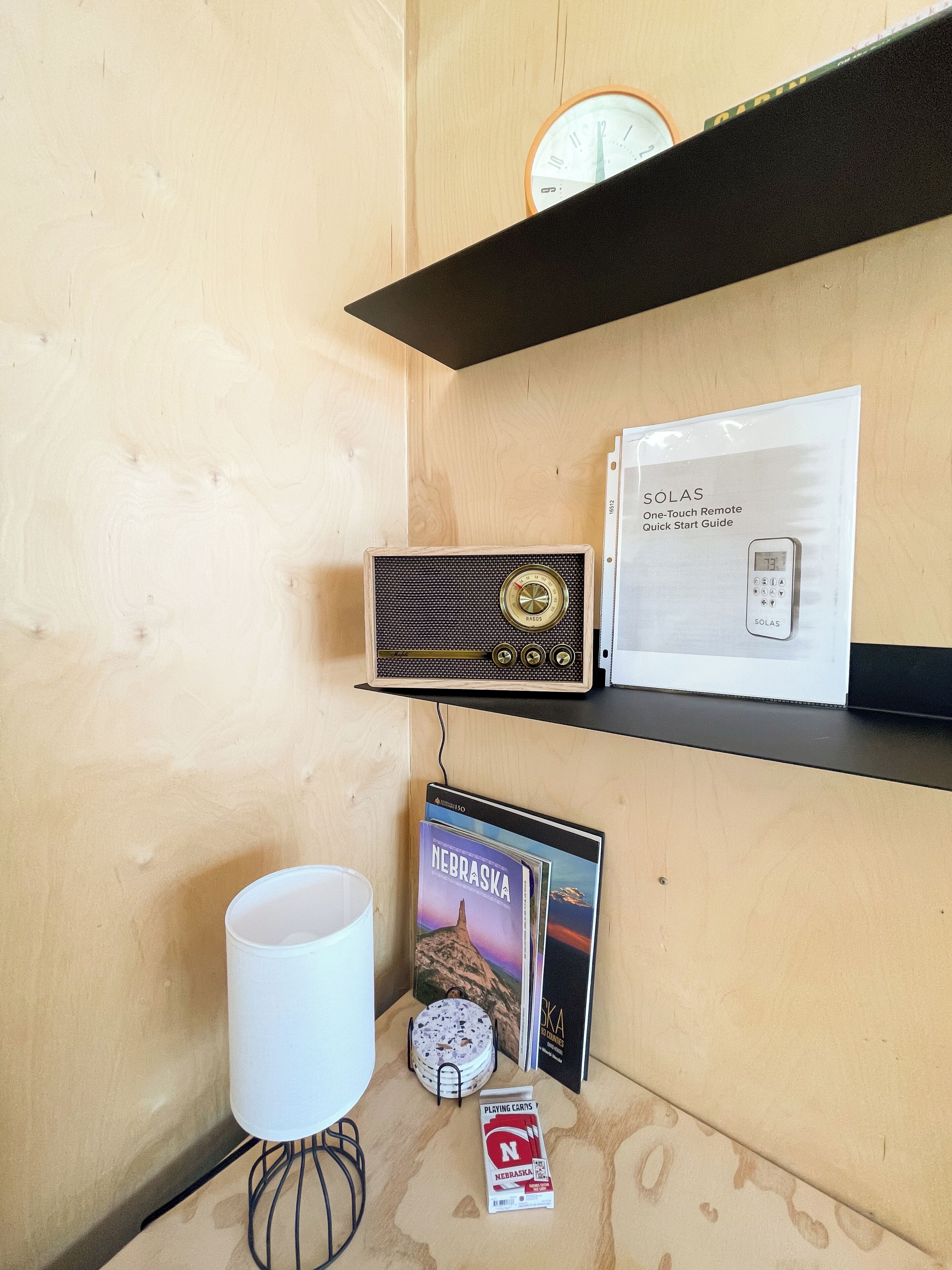 A wooden wall with a clock, a radio, a remote control, and some CDs.