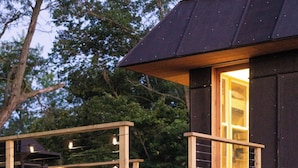 Une cabane en bois avec un toit sombre, une terrasse en bois et une fenêtre dotée d’un cadre en bois.