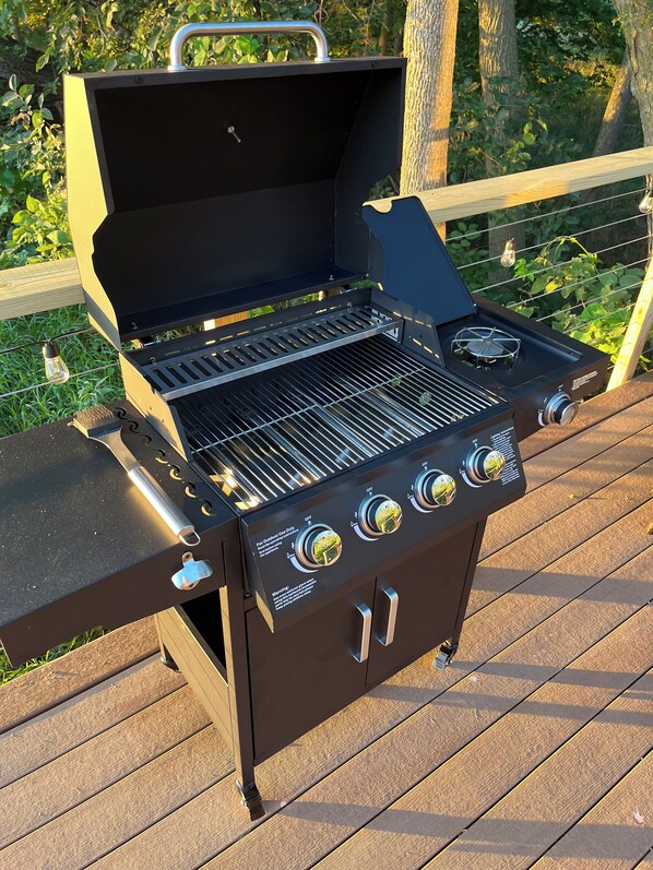 A black outdoor grill with four burners and a side burner, placed on a wooden deck.