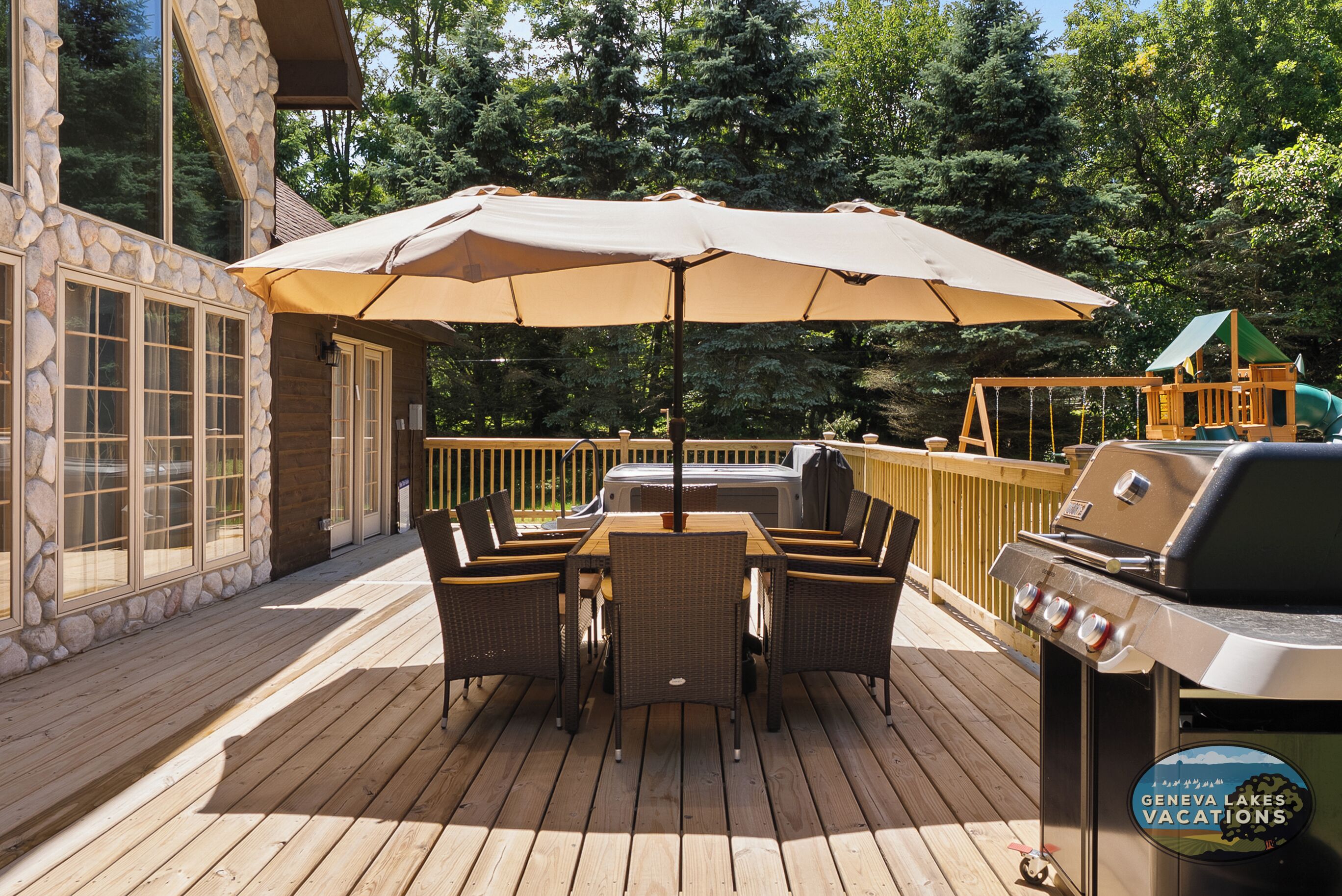 Une terrasse en bois avec une table et des chaises, un parasol et un barbecue.