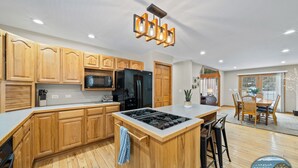 A modern kitchen with wooden cabinets, a central island, and a dining area with a table and chairs. - Hot Tub | 5 Minutes to Wilmot Ski Resort  | Game Room (Twin Lakes)