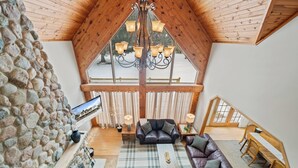 A high-ceilinged room with a stone wall, a chandelier, a fireplace, a sofa, and a dining table. - Hot Tub | 5 Minutes to Wilmot Ski Resort  | Game Room (Twin Lakes)
