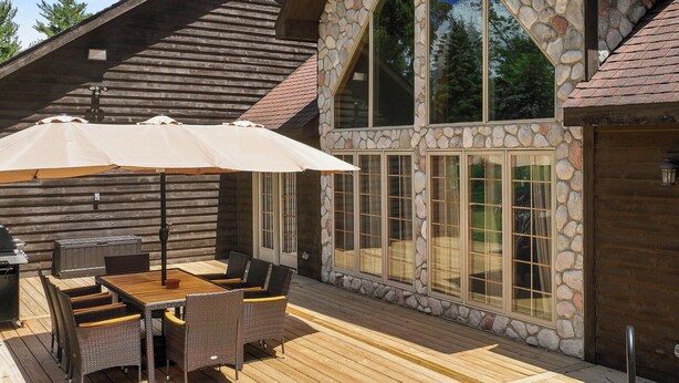 A wooden deck with a hot tub, outdoor furniture, and a stone wall with large windows. - Hot Tub | 5 Minutes to Wilmot Ski Resort  | Game Room (Twin Lakes)