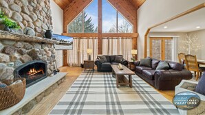 A cozy living room with a stone fireplace, leather sofas, and a large window offering a view of trees. - Hot Tub | 5 Minutes to Wilmot Ski Resort  | Game Room (Twin Lakes)