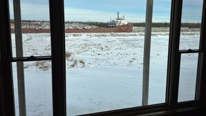 En vy genom ett fönster i en stor industribyggnad, med ett snötäckt landskap och ett fartyg i bakgrunden.