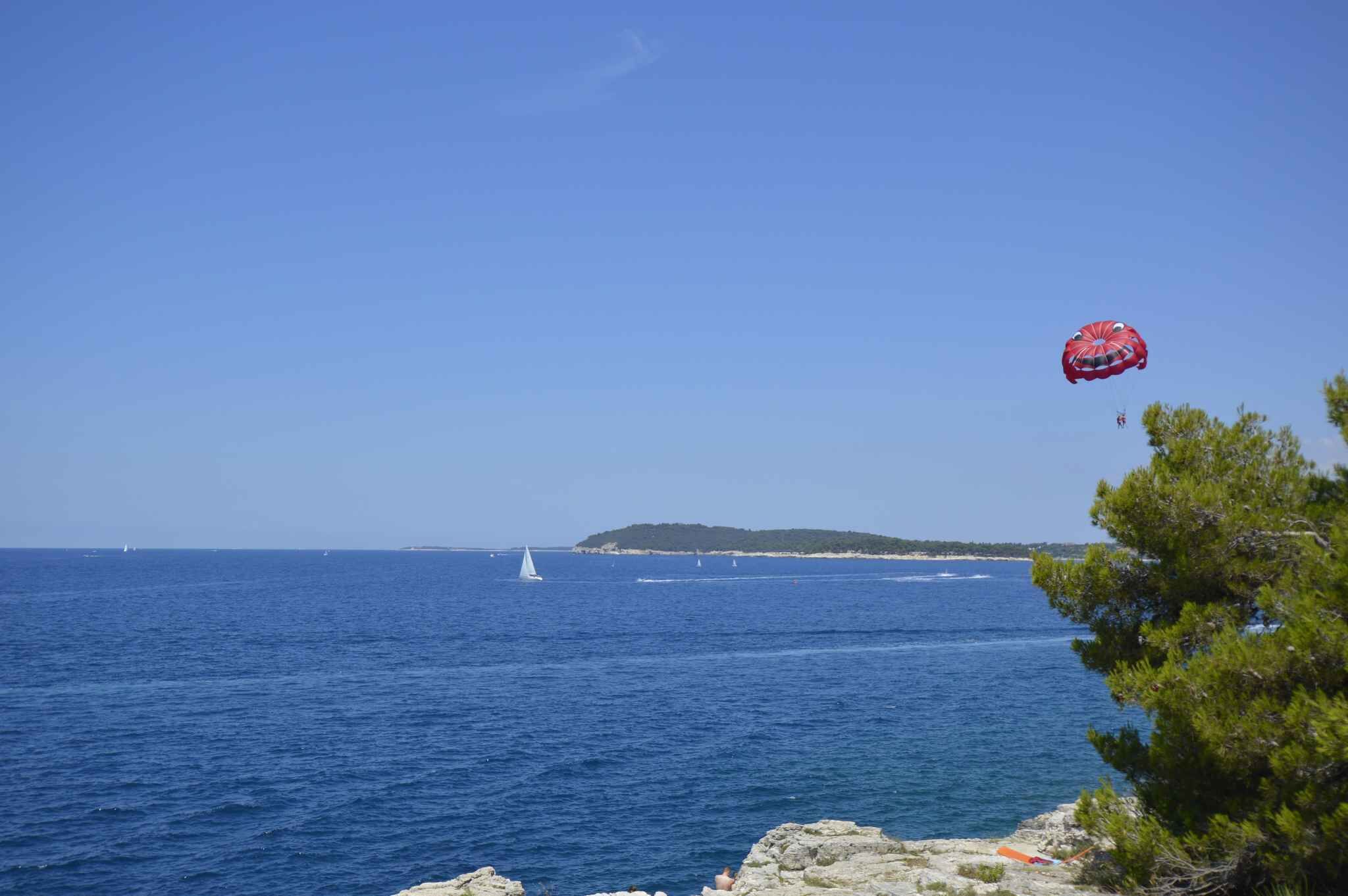 A coastal view with a clear sky, a sailboat, and a distant island.