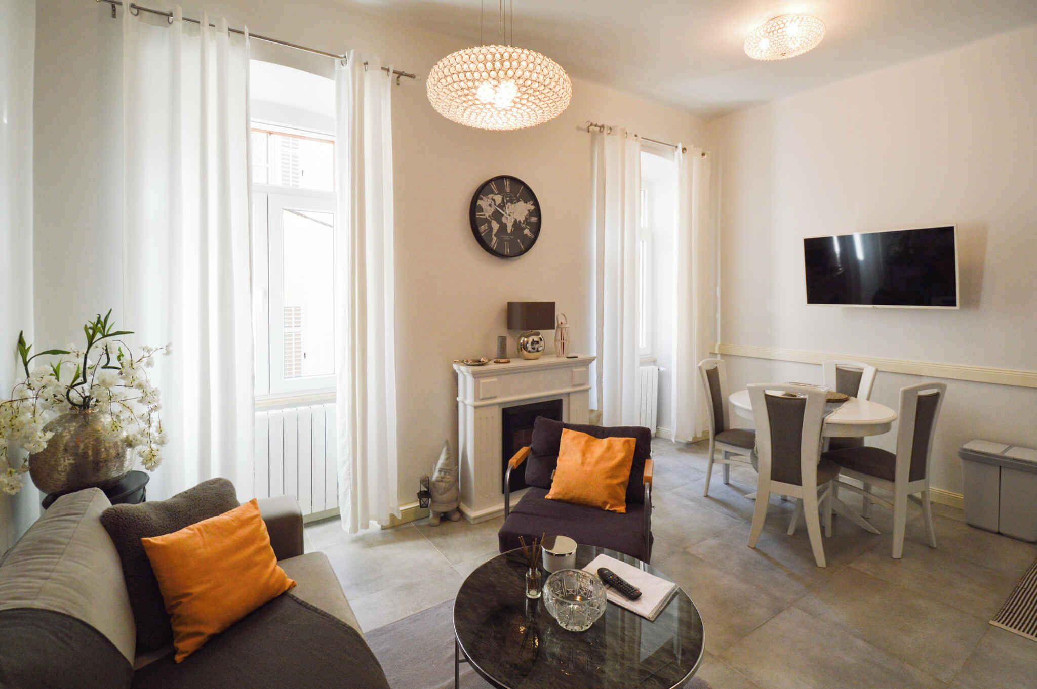 A living room with a sofa, a coffee table, a fireplace, a dining area with chairs, and a TV mounted on the wall.