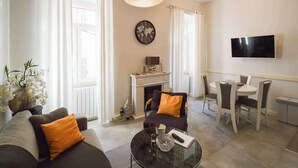 A living room with a sofa, a coffee table, a fireplace, a dining area with chairs, and a TV mounted on the wall. - Holiday apartment in the city centre (Pula)