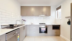 Una cocina moderna con azulejos blancos, electrodomésticos de acero inoxidable y armarios de color gris claro.