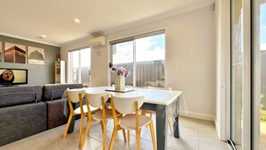Una sala de estar moderna con un sofá, una mesa de comedor con sillas, un televisor y un ventanal con vistas.