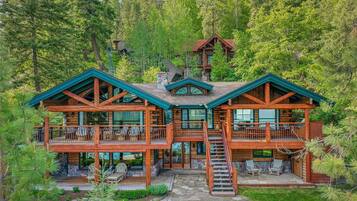 Une cabane en rondins avec un balcon au deuxième étage, des fondations en pierre et une forêt en arrière-plan.