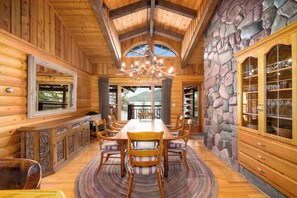 A wooden dining room with a large table, chairs, and a chandelier.