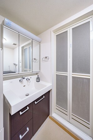 Un baño con lavamanos blanco, muebles oscuros, un espejo y una puerta de ducha de vidrio esmerilado.