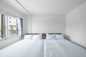 Habitación de hotel con una cama grande, una ventana con cortinas y vistas a edificios.