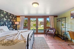 Un dormitorio con cama, una silla, un escritorio y vistas a través de un ventanal.