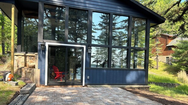 Ein modernes Haus mit großen Fenstern, einem Steinfundament und einer Ziegelterrasse.