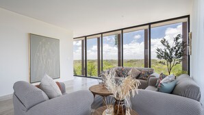 Ein modernes Wohnzimmer mit großen Fenstern, grauen Sofas und einem Couchtisch aus Holz mit einer Vase.